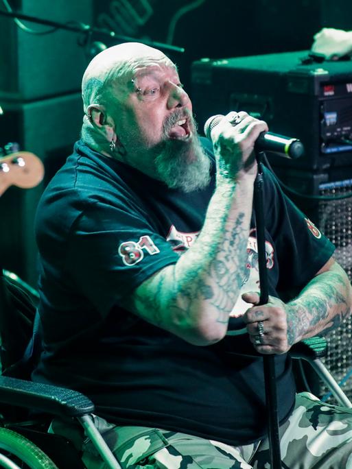 Paul Di'Anno sitzt in einem Rollstuhl auf der Bühne und singt.