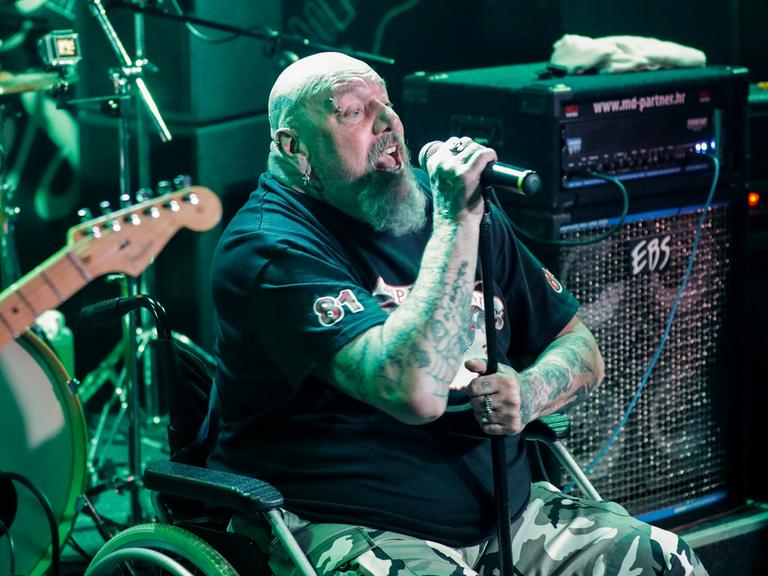 Paul Di'Anno sitzt in einem Rollstuhl auf der Bühne und singt.