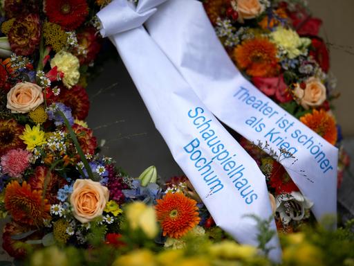 Ein Kranz mit Blumen und dem Schriftzug "Theater ist schoener schöner als Krieg"