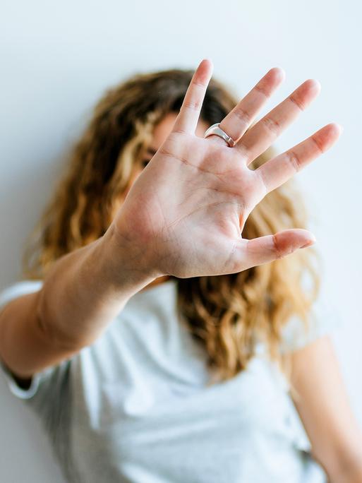 Porträt einer Frau, die ihre Hand abwehrend in die Kamera hält und dabei ihr Gesicht verdeckt
