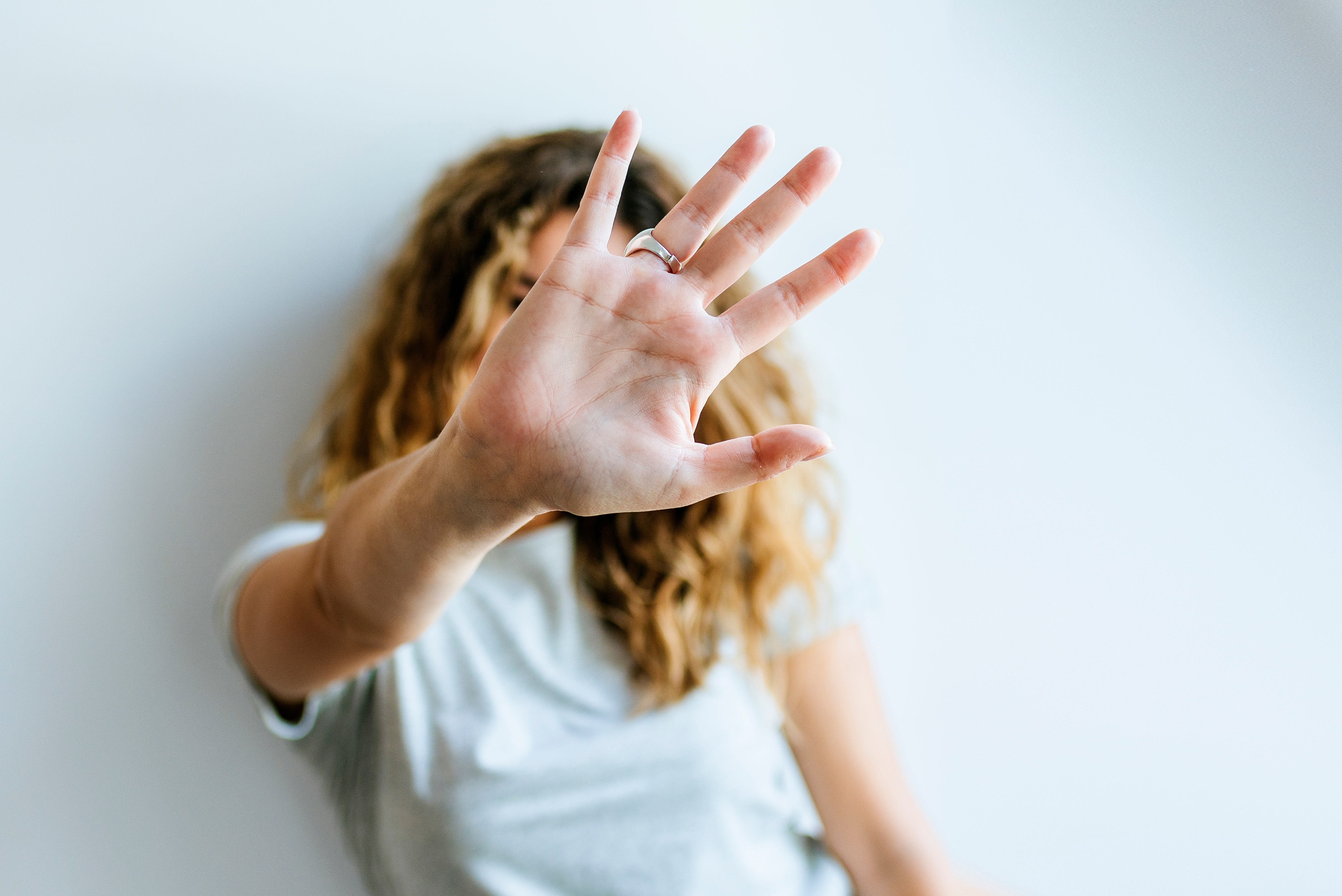 Porträt einer Frau, die ihre Hand abwehrend in die Kamera hält und dabei ihr Gesicht verdeckt