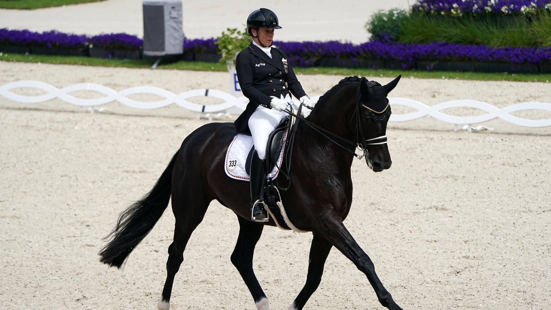 Isabell Werth auf ihrem schwarzen Pferd. Sie trägt eine weisse Hose und eine schwarze Jacke.