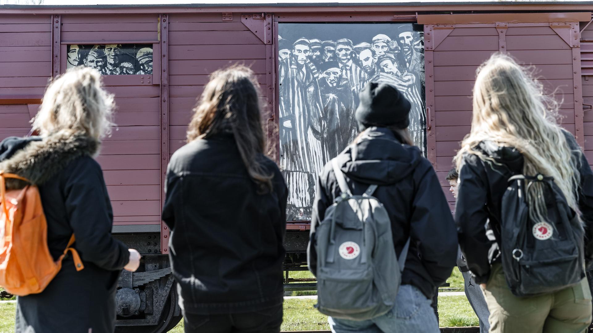 Schülerinnen betrachten auf einem Rundgang einen historischen Reichsbahnwaggon, der symbolisch für den ehemaligen Lagerbahnhof des Konzentrationslagers Neuengamme steht. 