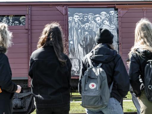 Schülerinnen betrachten auf einem Rundgang einen historischen Reichsbahnwaggon, der symbolisch für den ehemaligen Lagerbahnhof des Konzentrationslagers Neuengamme steht. 