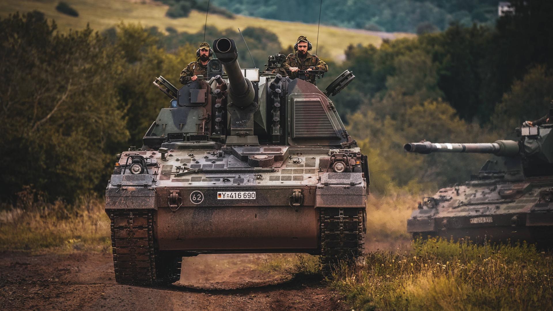 Zwei Soldaten der Bundeswehr fahren auf einer Panzerhaubitze während eines Manövers.