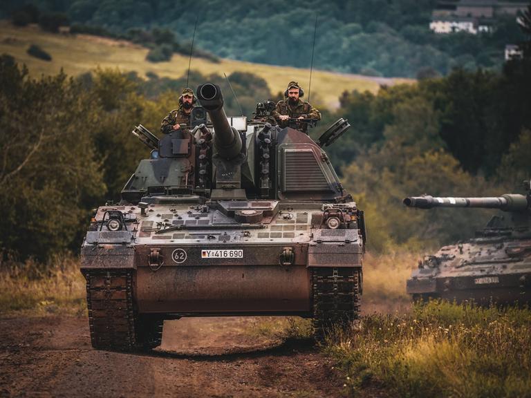 Zwei Soldaten der Bundeswehr fahren auf einer Panzerhaubitze während eines Manövers.