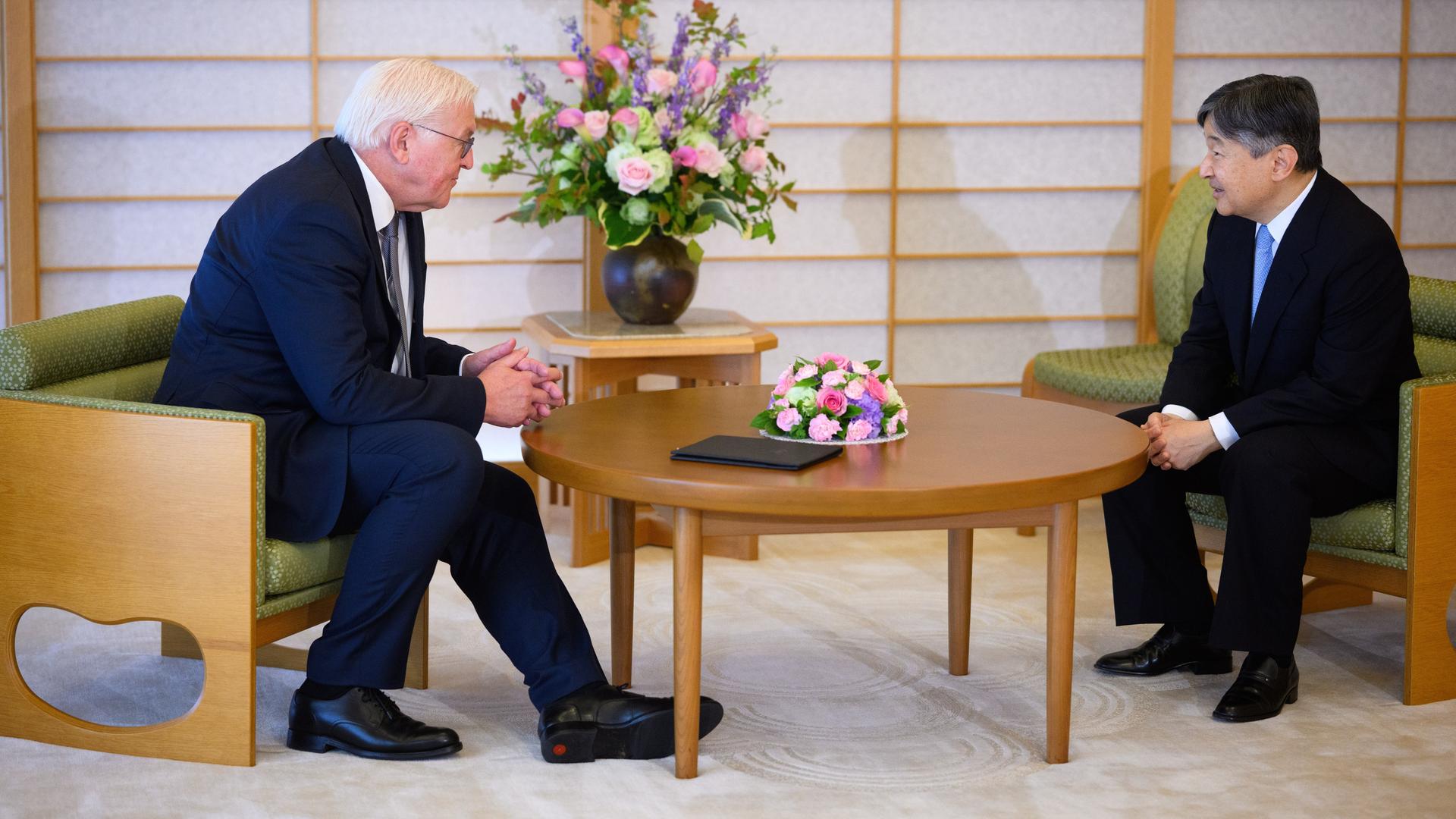 Frank-Walter Steinmeier und Kaiser Naruhito von Japan treffen sich zu einem Gespräch an einem Tisch im Kaiserpalast. Im Hintergrund steht ein Blumenstrauß.