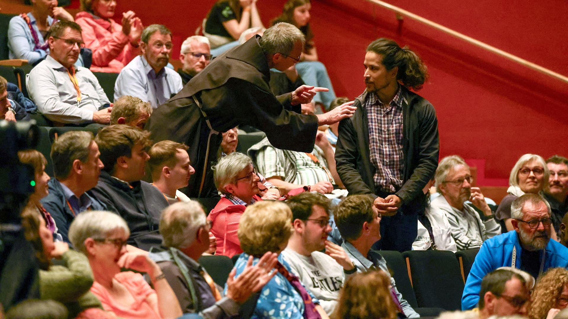 Erfurt: Ein Mönch spricht zu einem Demonstranten, während Bundeskanzler Scholz (SPD) auf dem Katholikentag in Erfurt an einer Podiusmdiskussion mit dem Titel "Gemeinschaft stärken - Gesellschaft gestalten.