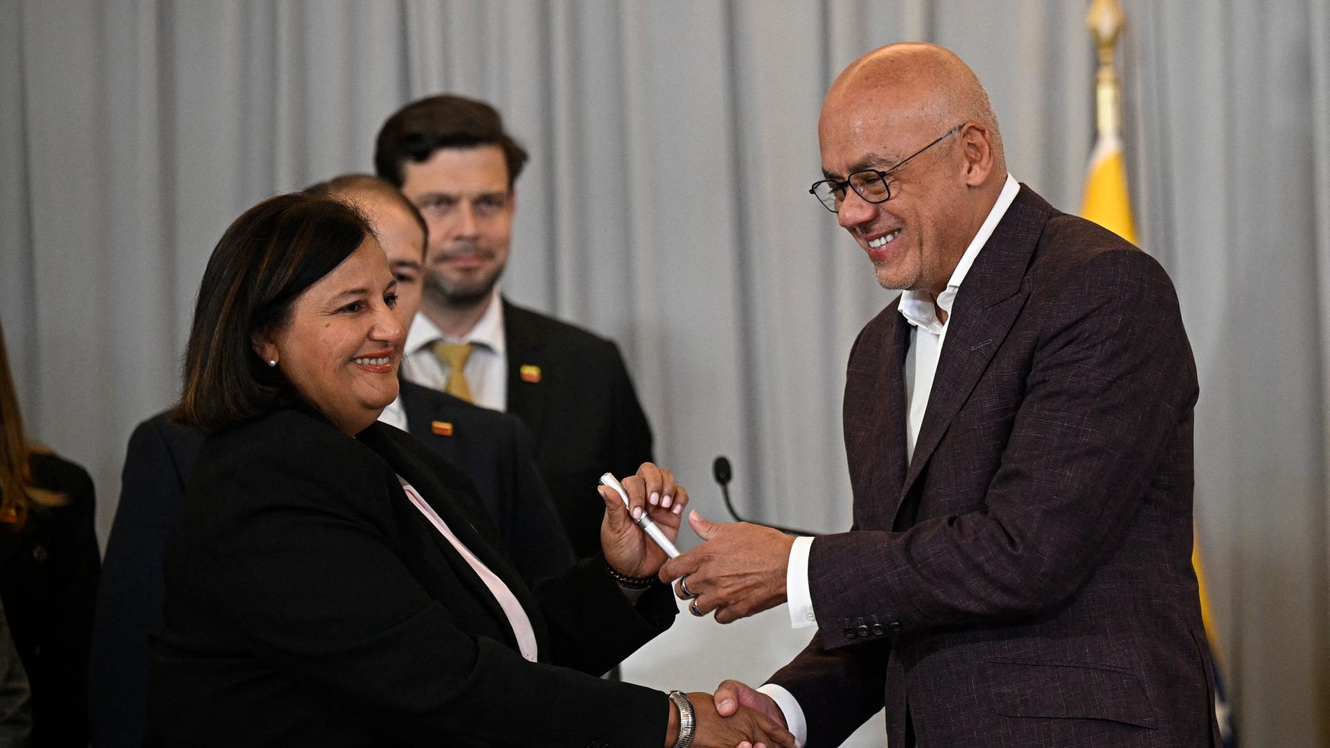 Die Leiterin der Oppositionsdelegation Dinorah Figuera (l) und Parlamentspräsident Jorge Rodriguez geben sich die Hand. Beide lächeln.