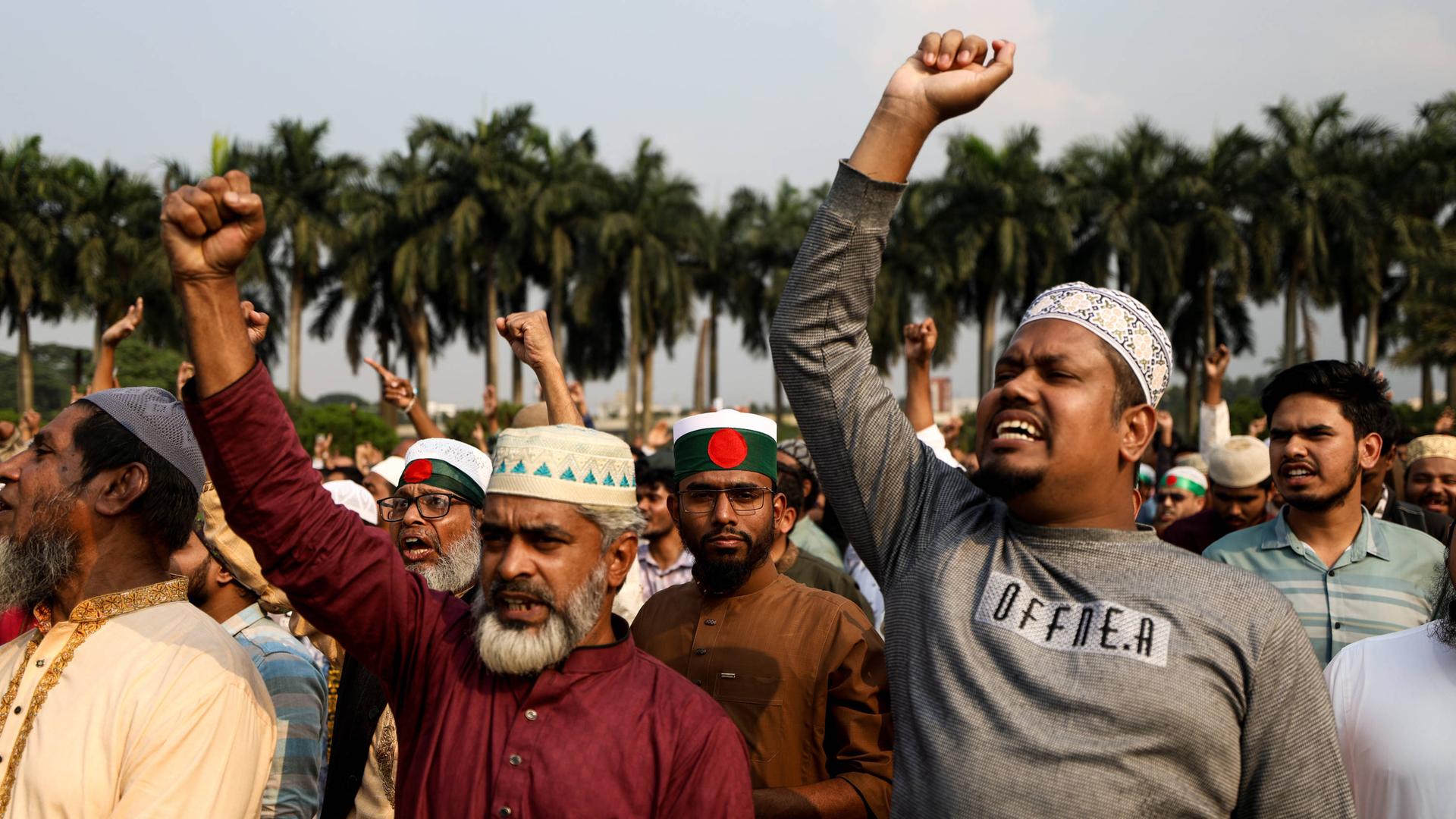 Eine große Gruppe von Männern steht auf einem Platz. Viele von ihnen erheben ihre Hände zur Faust. 