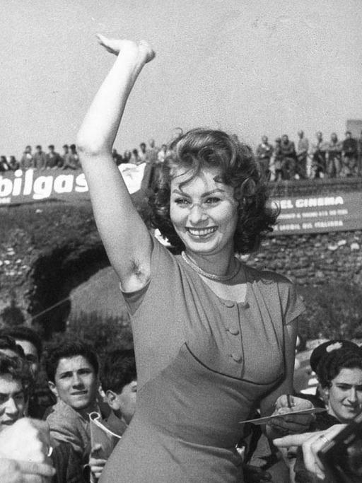 Die italienische Schauspielerin Sophia Loren winkt ihren Fans zu. Ihr rechter Arm ist in die Höhe gestreckt.