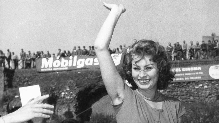 Die italienische Schauspielerin Sophia Loren winkt ihren Fans zu. Ihr rechter Arm ist in die Höhe gestreckt.