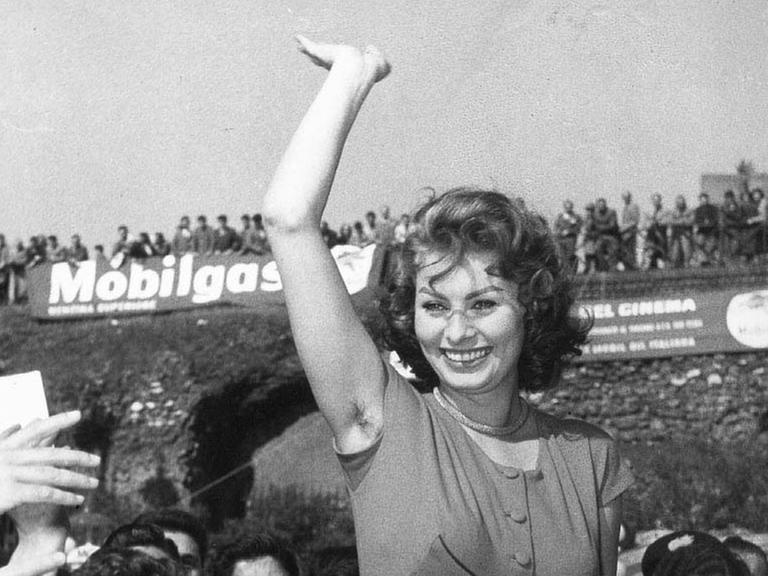 Die italienische Schauspielerin Sophia Loren winkt ihren Fans zu. Ihr rechter Arm ist in die Höhe gestreckt.