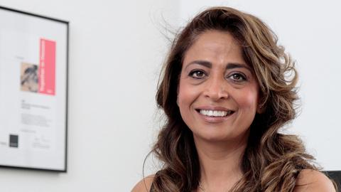 Nadia Qani sitzt am Schreibtisch in ihrem Büro und schaut freundlich in die Kamera.