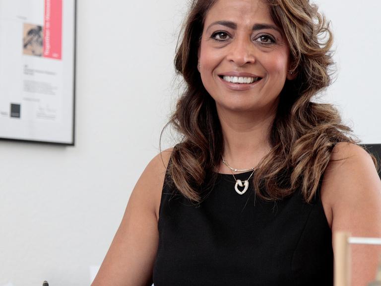 Nadia Qani sitzt am Schreibtisch in ihrem Büro und schaut freundlich in die Kamera.
