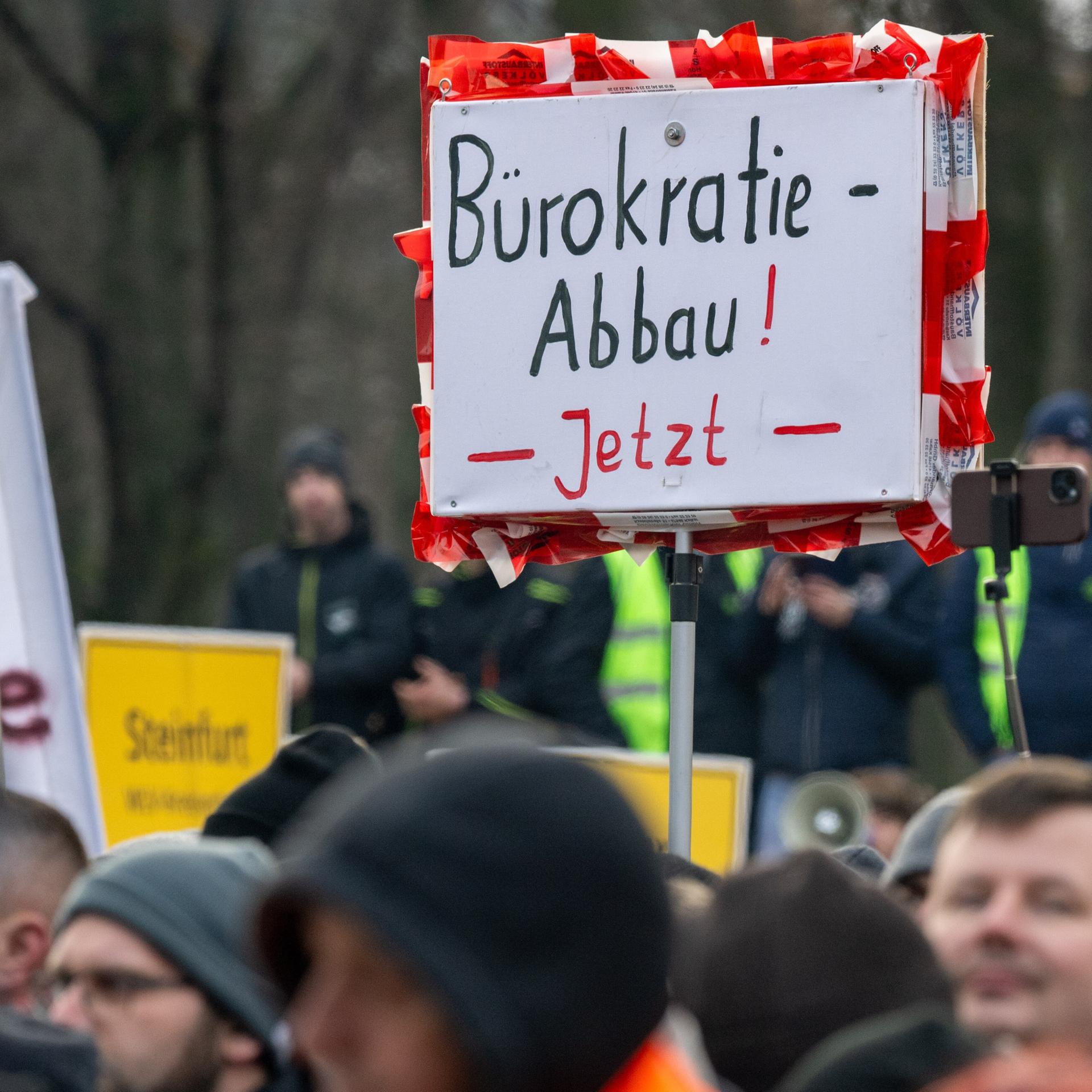 Bei einer Kundgebung hält jemand ein Schild mit der Aufschrift „Bürokratie-Abbau! Jetzt“ hoch.