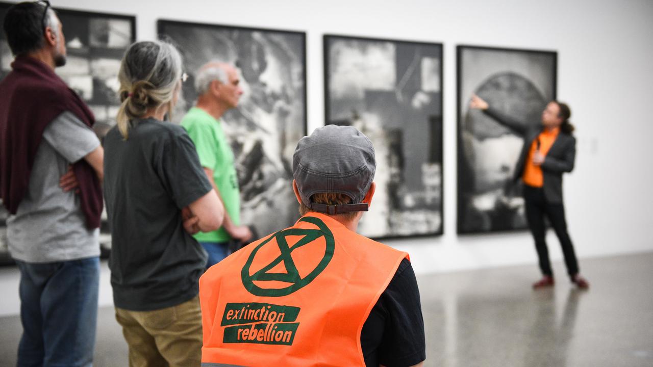 Führung im Musem Folkwang, im Vordergrund ist eine Person mit knalloranger "Extiction Rebellion"-Weste zu sehen, im Hintergrund eine Person, die ein Bild in der Ausstellung erläutert.