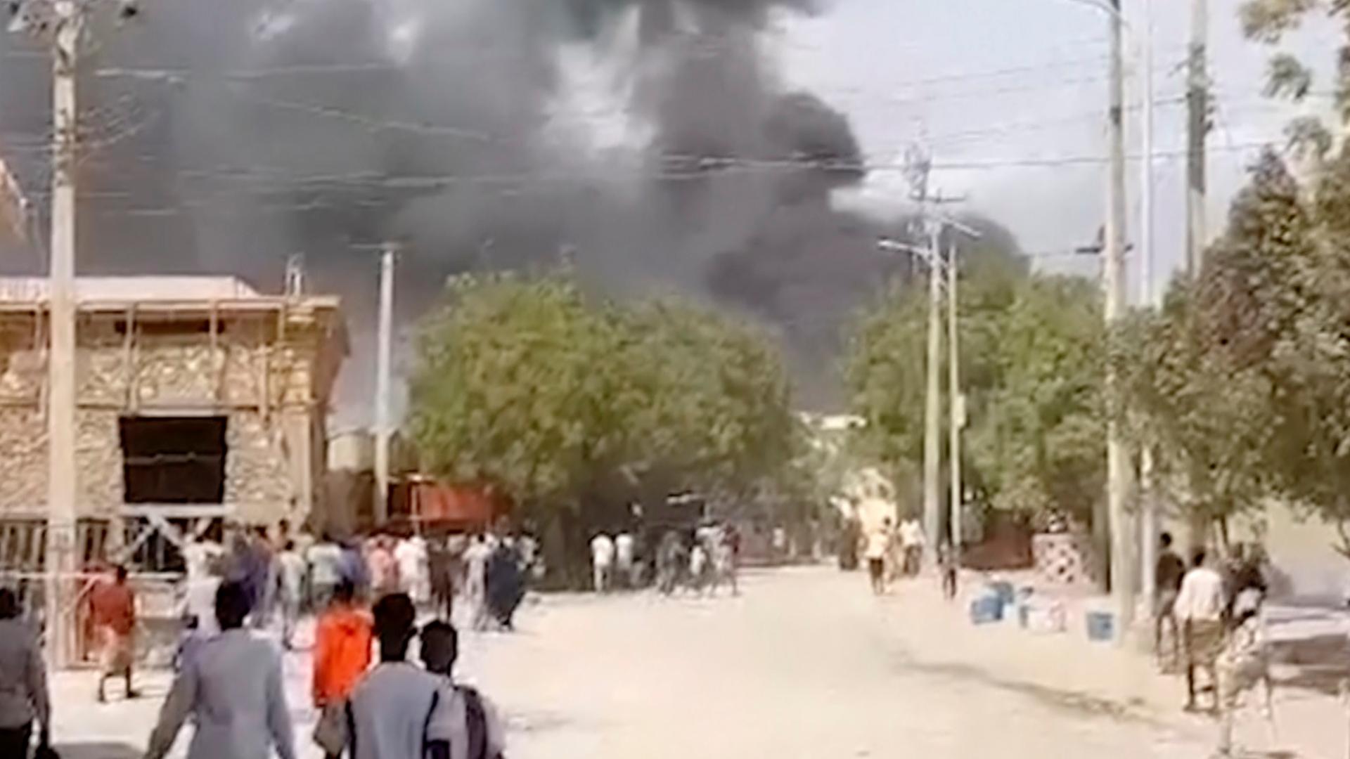 In dieser Aufnahme aus einem Video steigt Rauch nach einer Explosion auf. Im Vordergrund sind Menschen entlang einer Straße zu sehen. In dieser Aufnahme aus einem Video steigt Rauch nach einer Explosion auf. Im Vordergrund sind Menschen entlang einer Straße zu sehen.