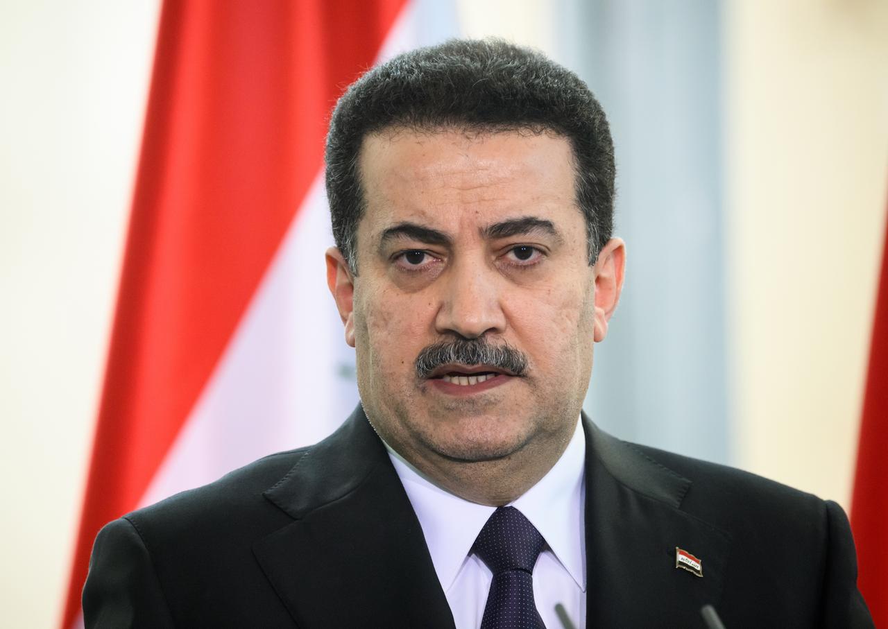 Porträt des irakischen Ministerpräsidenten Mohammed Schia al-Sudani bei einer Pressekonferenz. Im Hintergrund die Flagge des Irak.