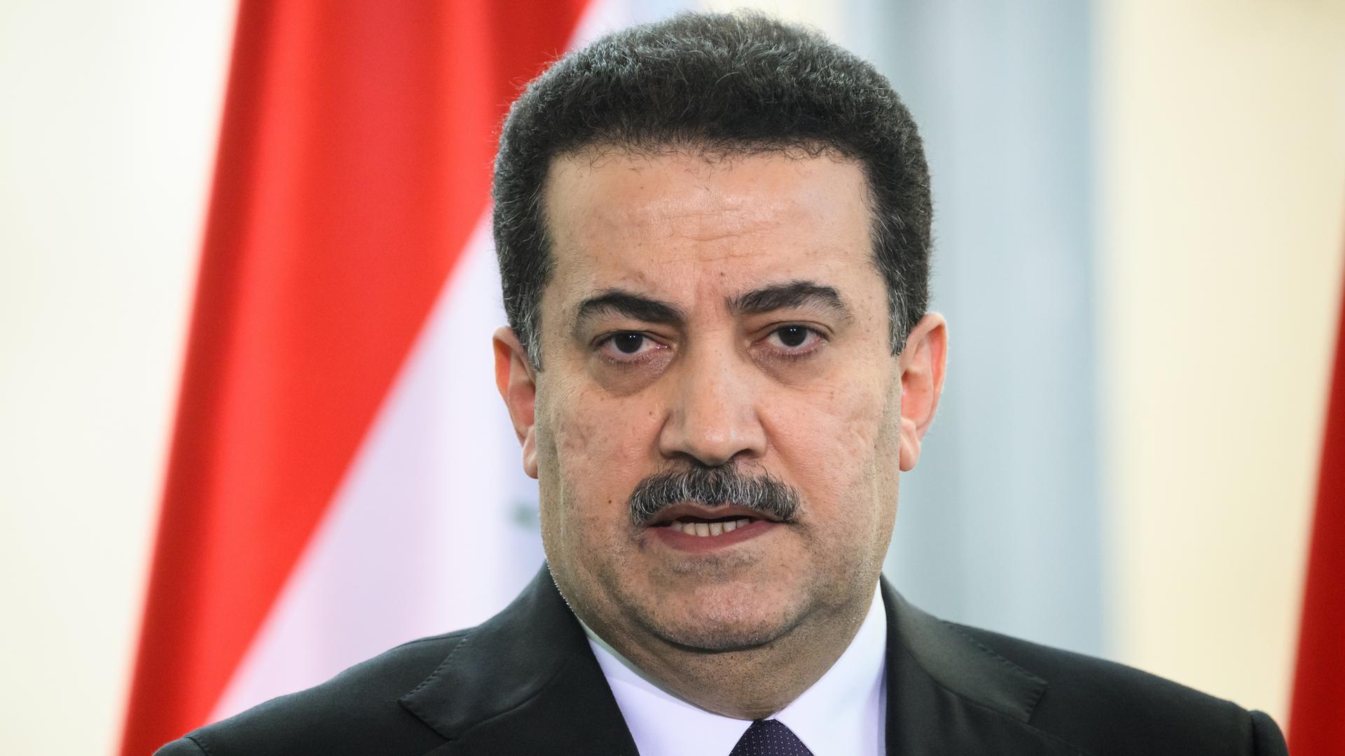 Porträt des irakischen Ministerpräsidenten Mohammed Schia al-Sudani bei einer Pressekonferenz. Im Hintergrund die Flagge des Irak.