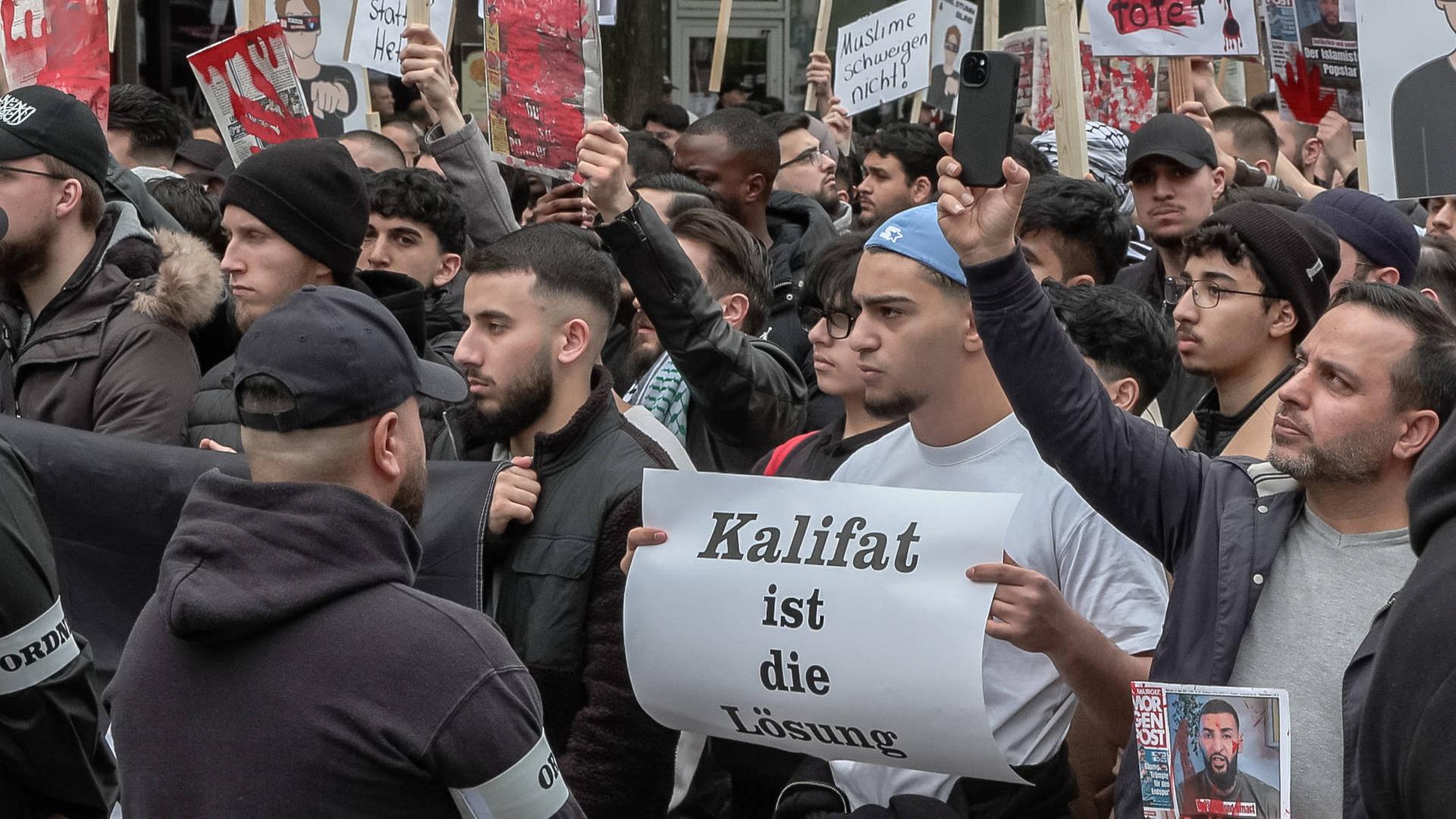 Junge muslimische Männer bei einer Islamisten-Demo in Hamburg. Auf einem Schild steht "Kalifat ist die Lösung".