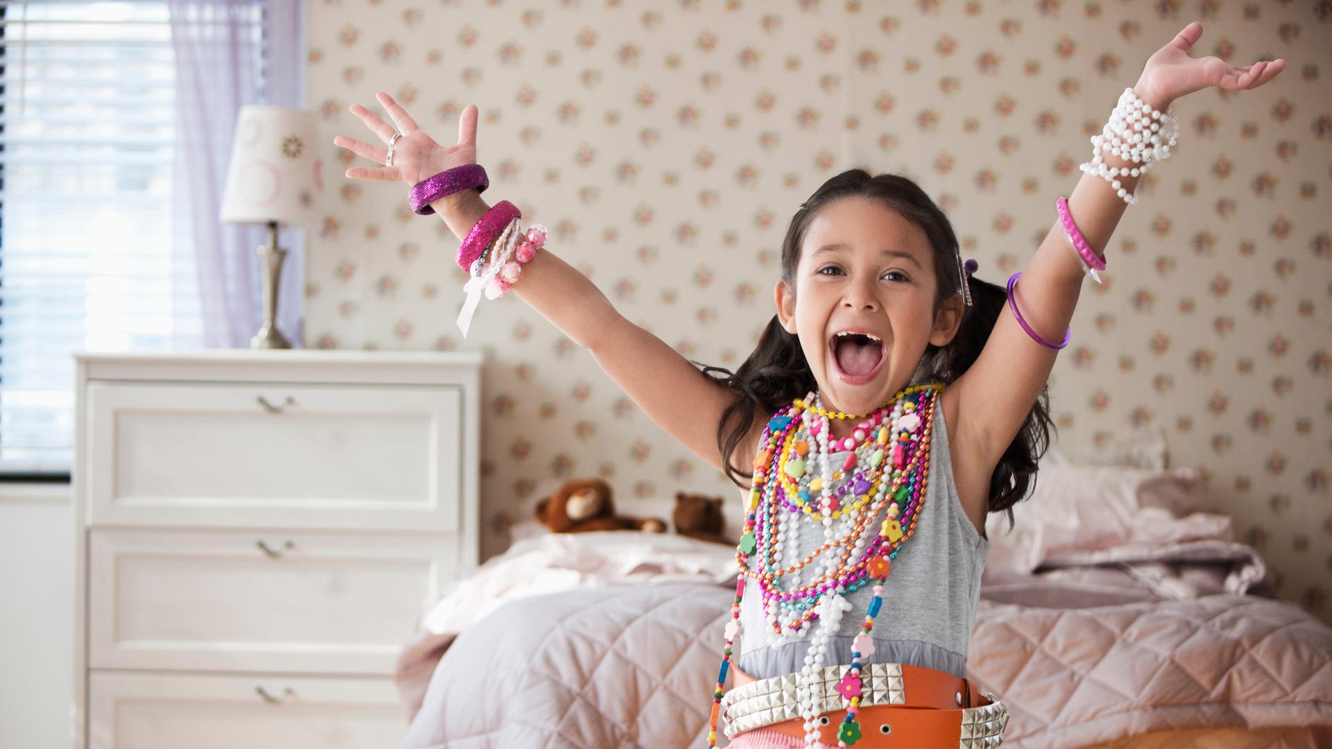 Mädchen mit vielen Glasperlenketten behangen zeigt stolz ihr Kinderzimmer