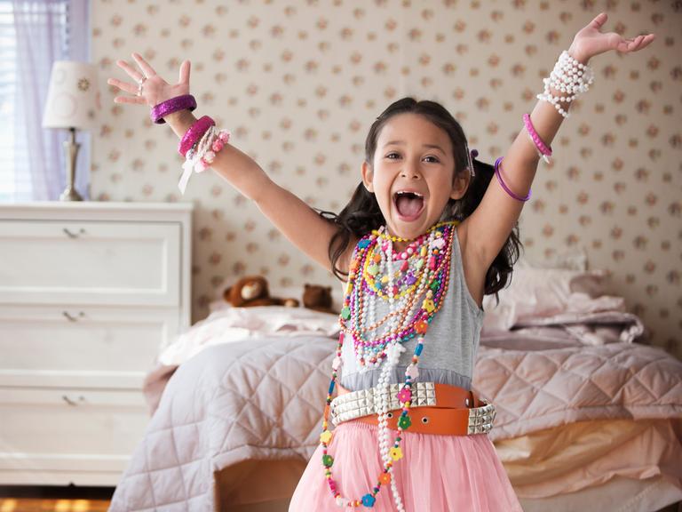 Mädchen mit vielen Glasperlenketten behangen zeigt stolz ihr Kinderzimmer