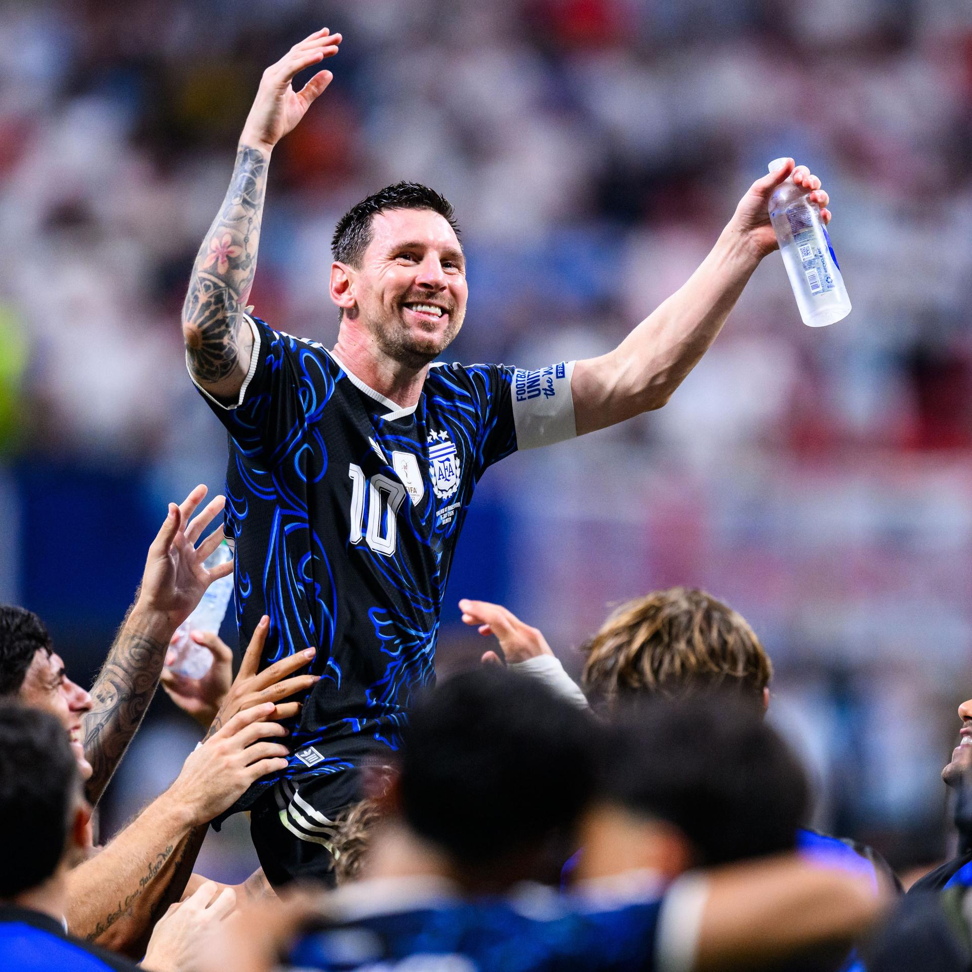 Der Fußball-Spieler von Argentinien Lionel Messi freut sich. Er hat beide Arme noch oben gestreckt. Seine Mit-Spieler heben Lionel Messi hoch.