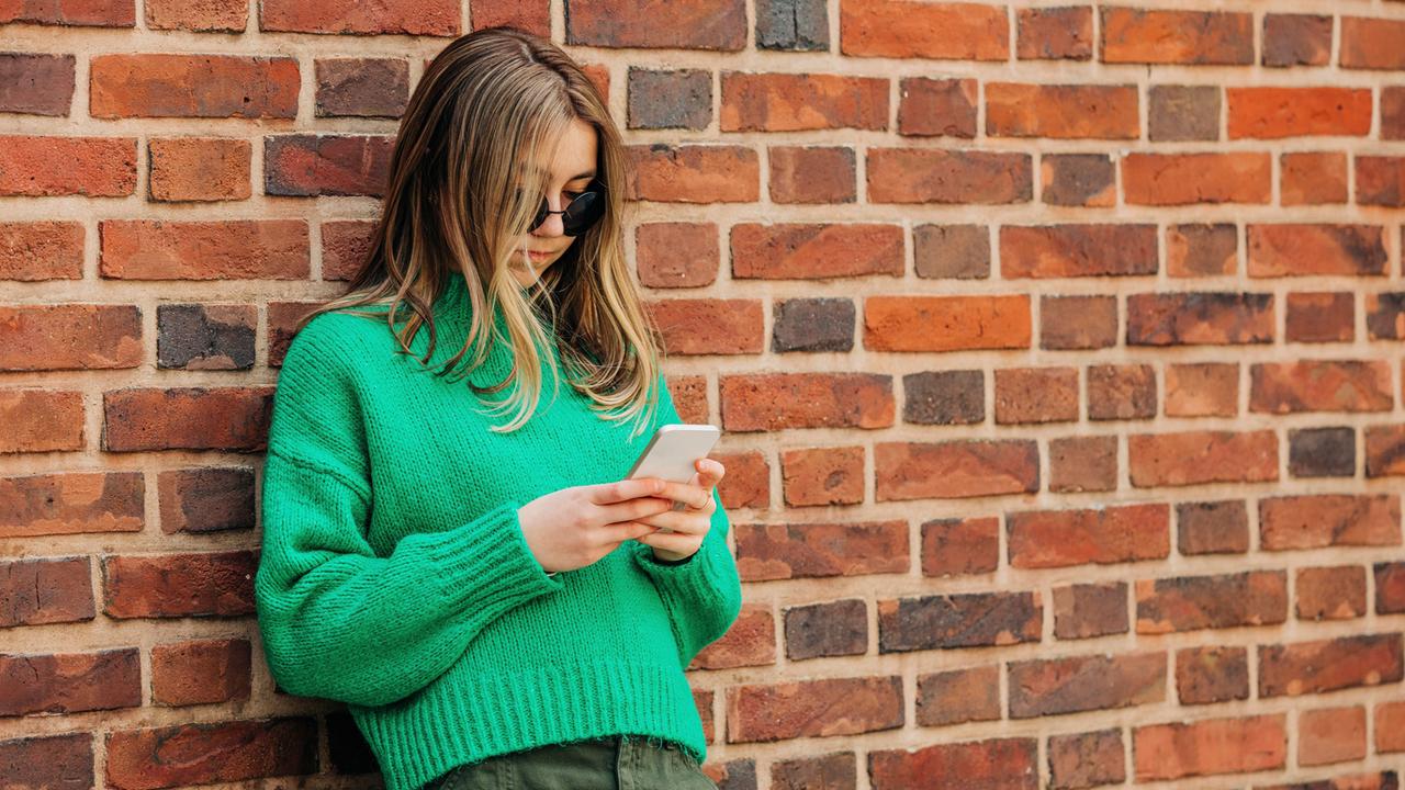 Ein Teenagerin lehnt an einer Wand und nutzt ihr Smartphone.