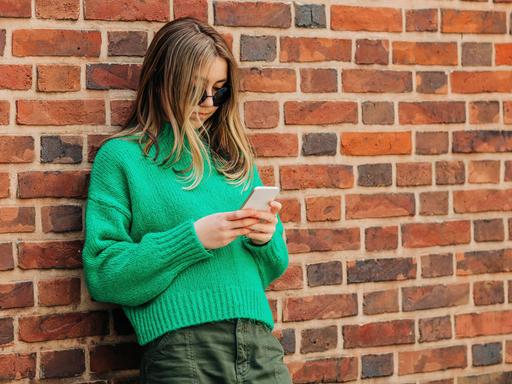 Ein Teenagerin lehnt an einer Wand und nutzt ihr Smartphone.