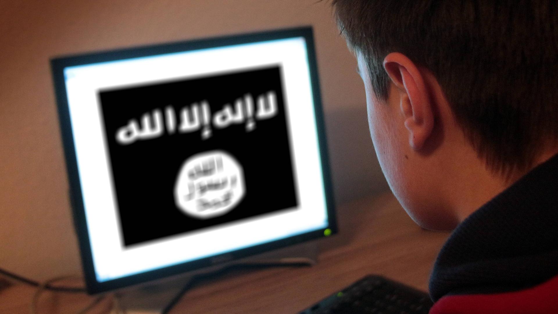 Ein Jugendlicher schaut auf einen Computerbildschirm, auf dem die Flagge des Islamischen Staates abgebildet ist.