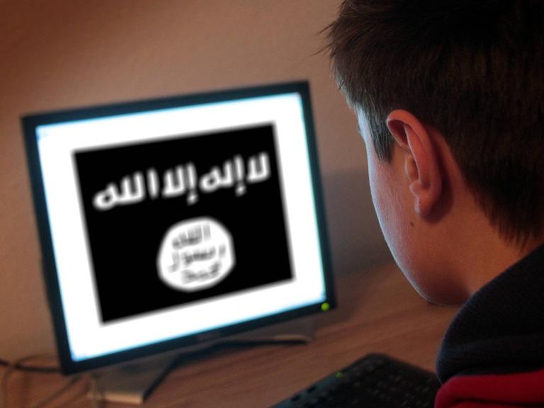 Ein Jugendlicher schaut auf einen Computerbildschirm, auf dem die Flagge des Islamischen Staates abgebildet ist.