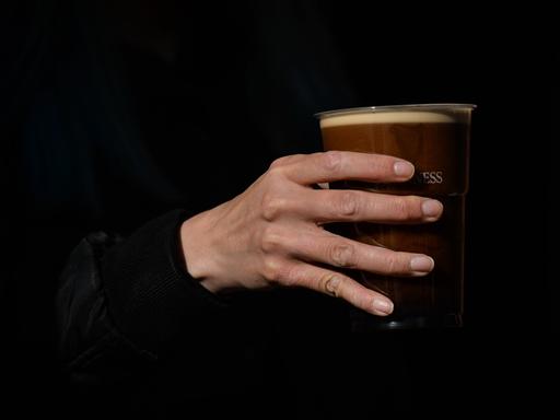 Eine Hand hält einen Plastikbecher mit dunklem Bier.
