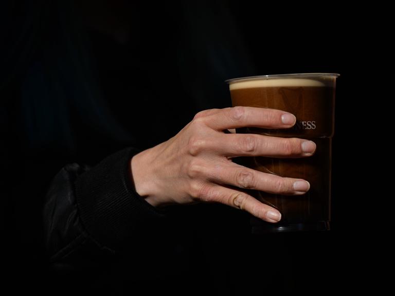Eine Hand hält einen Plastikbecher mit dunklem Bier.