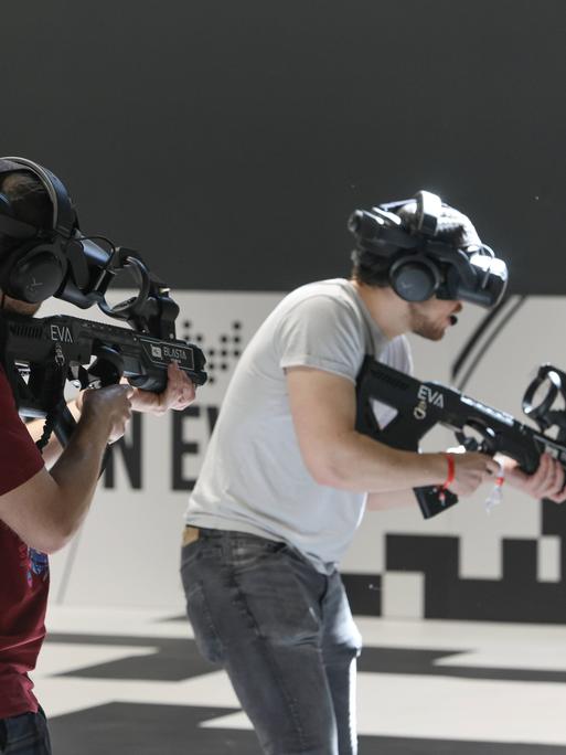 Zwei Männer spielen ein Shooter-Game während  der Messe Gamescom. Sie tragen Gewehre.