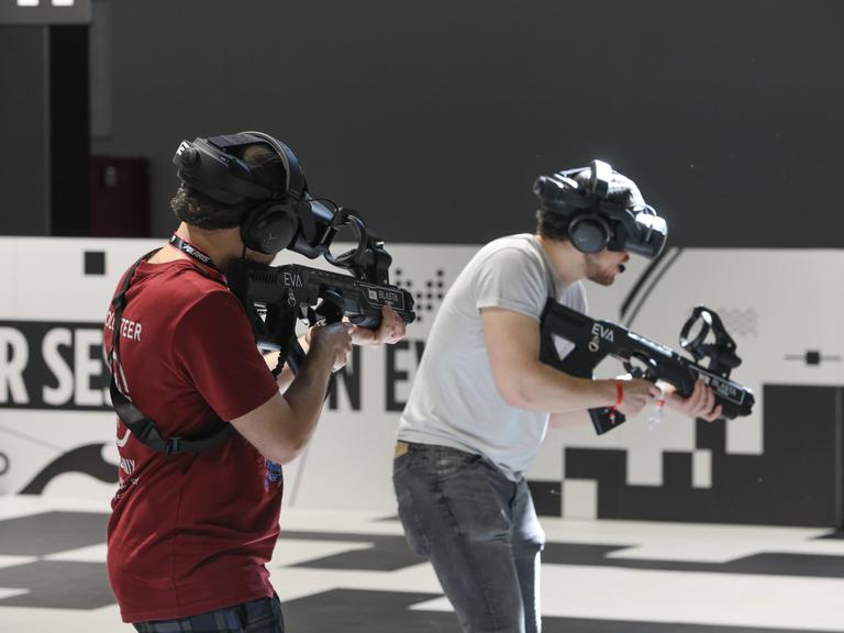 Zwei Männer spielen ein Shooter-Game während  der Messe Gamescom. Sie tragen Gewehre.