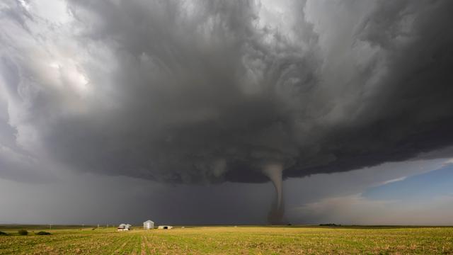 Ein Tornado über einem Feld. Im Vordergrund stehen Häuser.