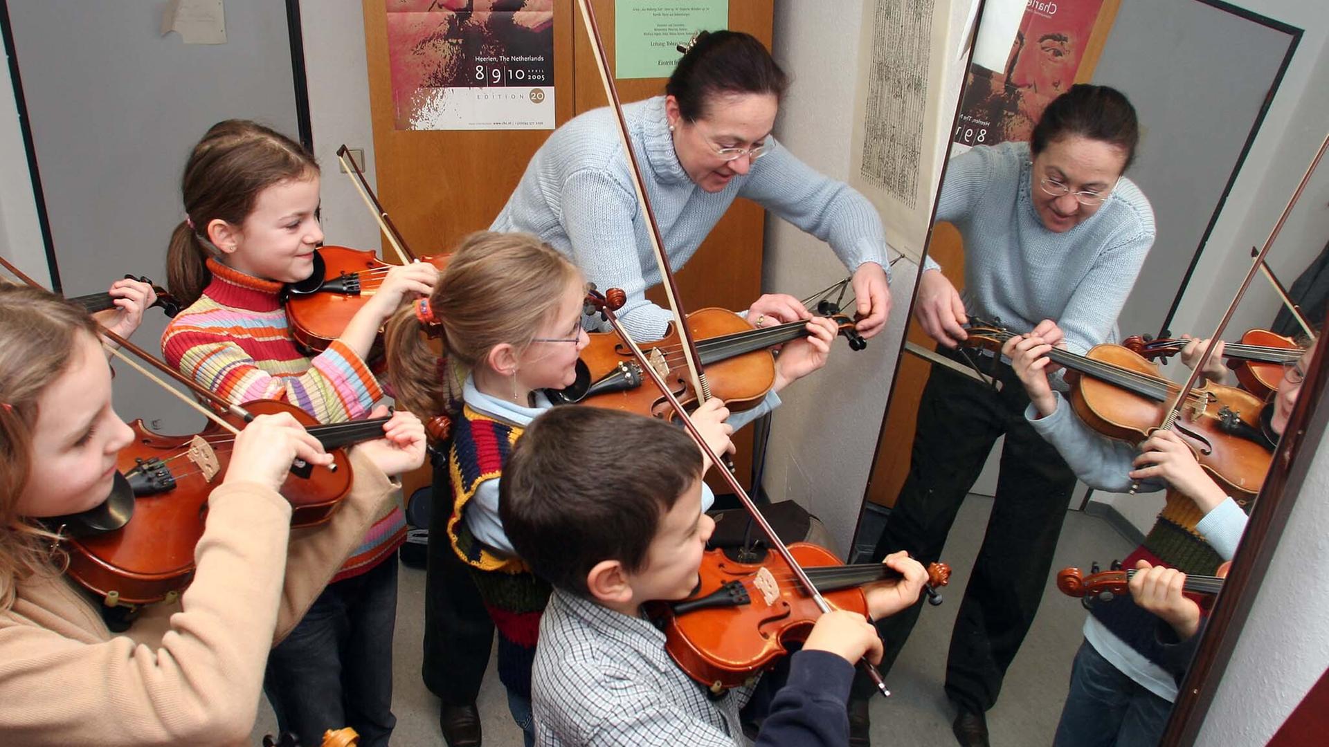 Geigenlehrerin erklärt am den kleinsten Geigenschülern vor dem Spiegel die richtige Haltung des Instruments. Geigenlehrerin erklärt am den kleinsten Geigenschülern vor dem Spiegel die richtige Haltung des Instruments.
