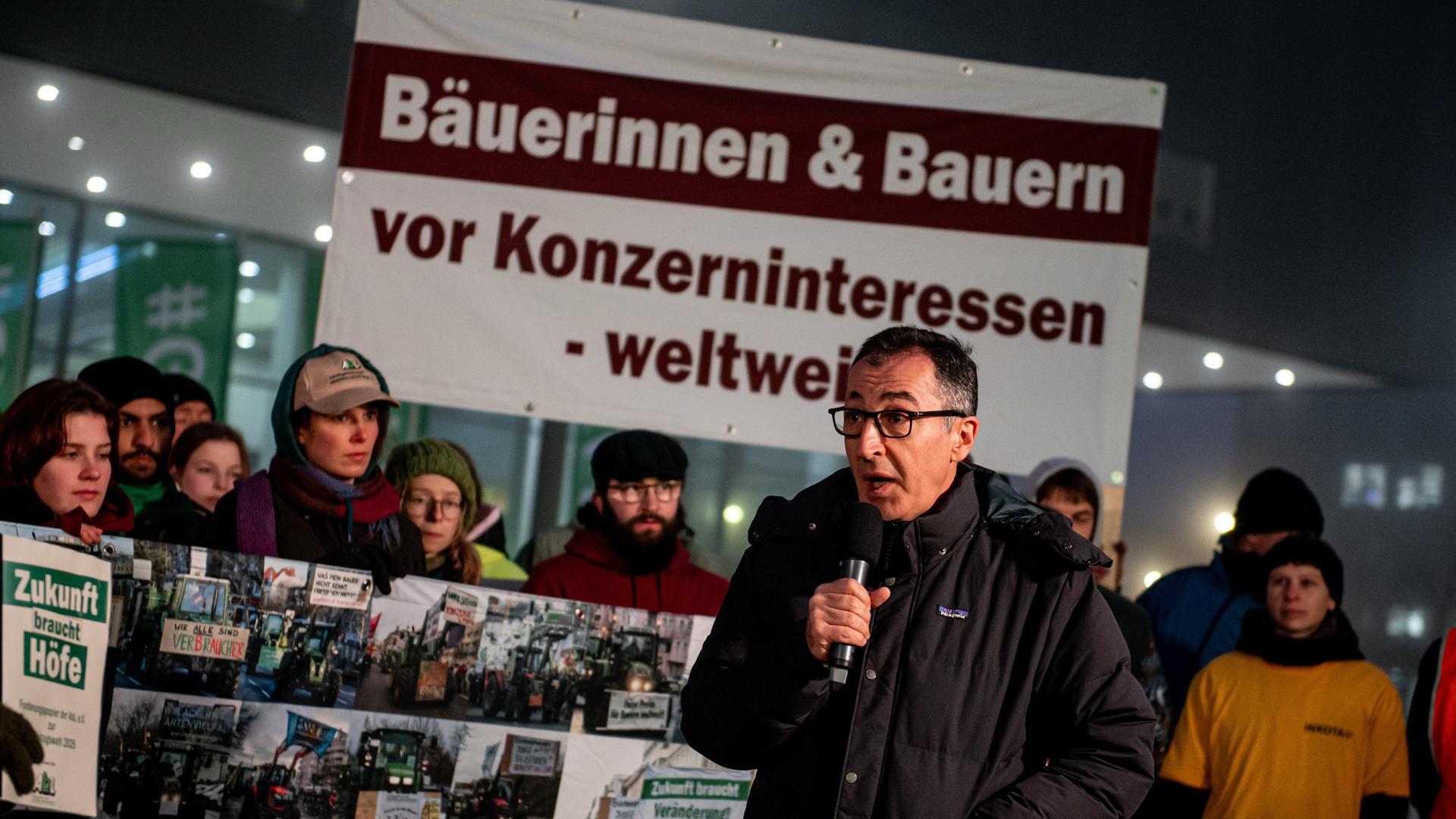 Landwirtschaftsminister Özdemir bei der Übergabe einer Protestnote des Bündnisses "Wir haben es satt!". Er steht vor einem Schild mit der Aufschrift "Bäuerinnen und Bauern vor Konzerninteressen weltweit" vor dem Messegelände in Berlin.