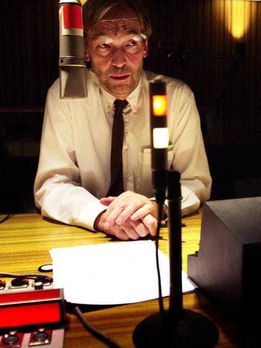 Wir sehen einen Mann, der in einem Radiostudio sitzt und einen Text einsprechen möchte. 