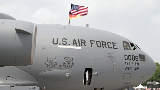 Das Foto zeigt ein graues Transport-Militärflugzeug am Boden. Das Flugzeug trägt die schwarze Aufschrift „U.S. Air Force“. Auf dem Flugzeug sind die Flaggen der USA und Deutschlands angebracht. 