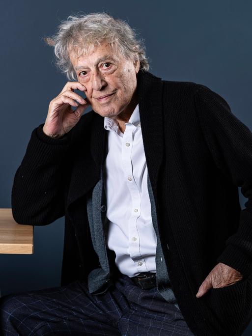 Der britische Dramatiker Tom Stoppard sitzt seitlich an einem Tisch, stützt den rechten Ellenbogen auf die Tischkante und fast sich mit der rechten Hand an die rechte Wange Der britische Dramatiker Tom Stoppard sitzt seitlich an einem Tisch, stützt den rechten Ellenbogen auf die Tischkante und fast sich mit der rechten Hand an die rechte Wange