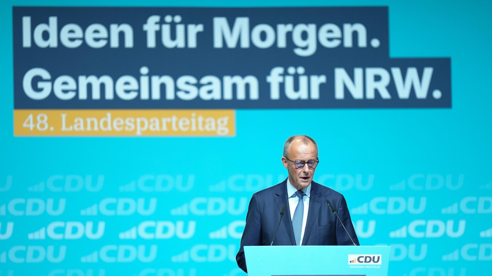 Merz ist am unteren Bildrand an einem Rednerpult zu sehen, er spricht. Dahinter groß eine blau-gelbe LED-Wand mit den Zeilen "Ideen für morgen. Gemeinsam für NRW. 48. Landesparteitag." Merz ist am unteren Bildrand an einem Rednerpult zu sehen, er spricht. Dahinter groß eine blau-gelbe LED-Wand mit den Zeilen "Ideen für morgen. Gemeinsam für NRW. 48. Landesparteitag."