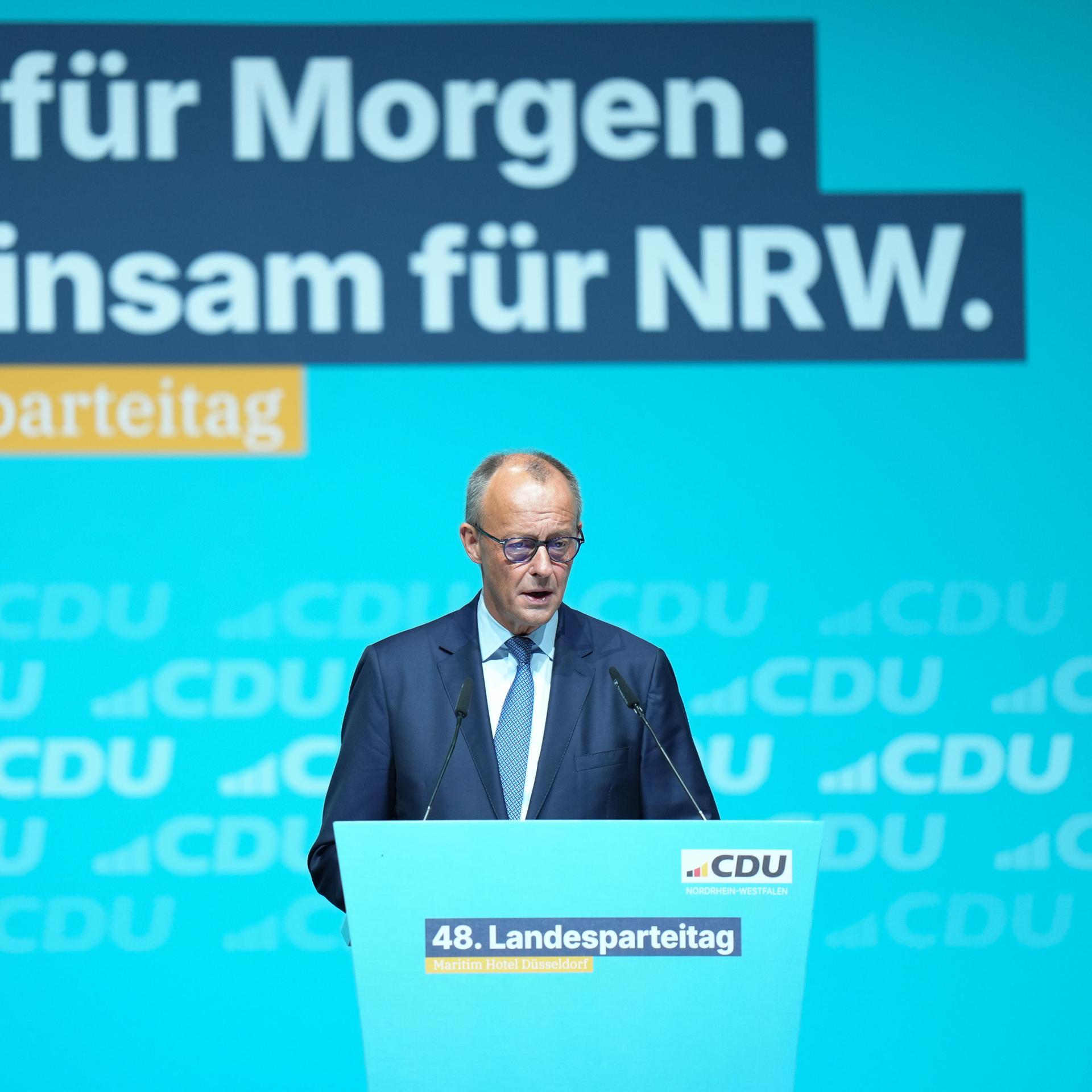 Merz ist am unteren Bildrand an einem Rednerpult zu sehen, er spricht. Dahinter groß eine blau-gelbe LED-Wand mit den Zeilen "Ideen für morgen. Gemeinsam für NRW. 48. Landesparteitag."