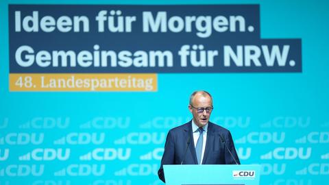 Merz ist am unteren Bildrand an einem Rednerpult zu sehen, er spricht. Dahinter groß eine blau-gelbe LED-Wand mit den Zeilen "Ideen für morgen. Gemeinsam für NRW. 48. Landesparteitag."