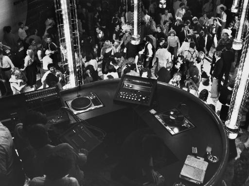 Blick auf einen DJ-Booth von oben, darunter eine große Tanzfläche.