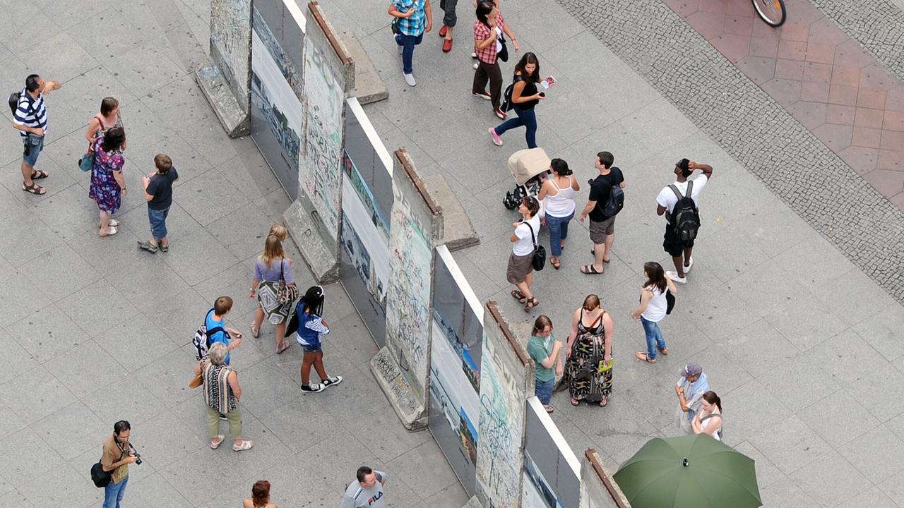 Besucher stehen auf beiden Seiten um einen historischen Teil der Berliner Mauer auf dem Potsdamer Platz herum. Besucher stehen auf beiden Seiten um einen historischen Teil der Berliner Mauer auf dem Potsdamer Platz herum.