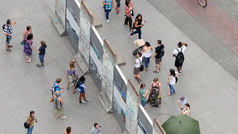 Besucher stehen auf beiden Seiten um einen historischen Teil der Berliner Mauer auf dem Potsdamer Platz herum. Besucher stehen auf beiden Seiten um einen historischen Teil der Berliner Mauer auf dem Potsdamer Platz herum.