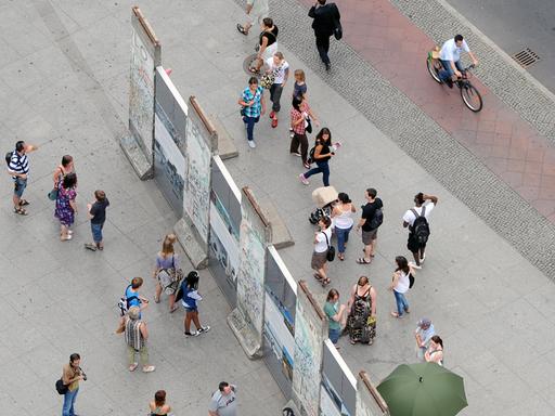Besucher stehen auf beiden Seiten um einen historischen Teil der Berliner Mauer auf dem Potsdamer Platz herum.