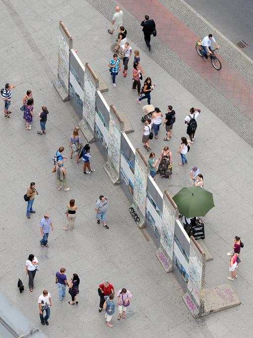 Besucher stehen auf beiden Seiten um einen historischen Teil der Berliner Mauer auf dem Potsdamer Platz herum.